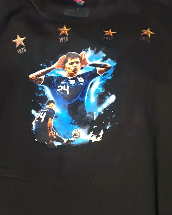 Remera negra con la estampa de un jugador de la selección argentina festejando, en tonos azules, con cuatro estrellas doradas.